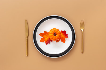 Festive Thanksgiving table setting with pumpkin in plate and cutlery - autumn leaves decorated on brown background, flat lay. Top viewの写真素材