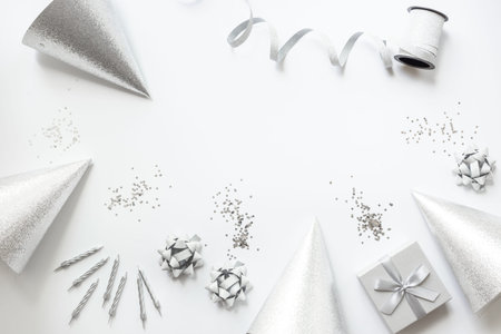 Frame of festive party decoration with silver streamers and gift box and carnaval caps on white background, top viewの写真素材