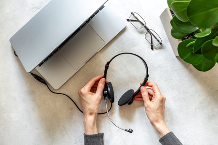 Top view of business office desk with hands holding headphones near laptop. Online conference. Call center work space.の写真素材