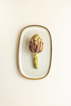 One artichoke flower - purple edible bud on a plate top view. Vegetables food ready to cook.の写真素材