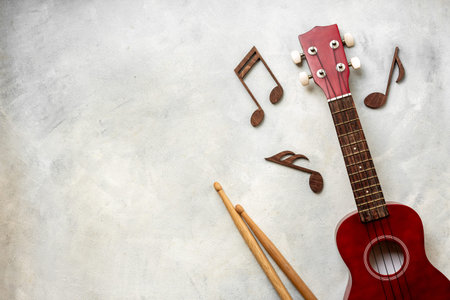 Red small guitar ukulele with drumsticks. Musical instruments, top view.