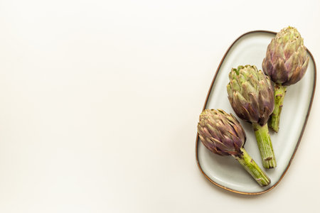 Tree heads of purple artichokes on a plate top view. Vegetables food ready to cook.の写真素材