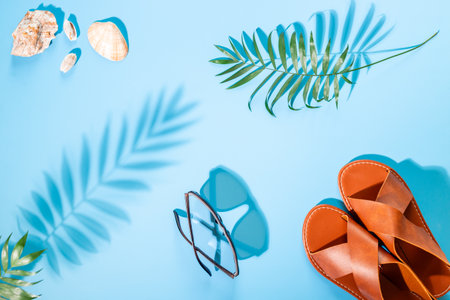 Vacation beach accessories with sunlight shadows. Sandals and tropical leaves, top view.の写真素材