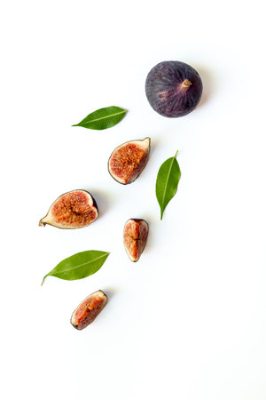 Purple ripe figs fruit and slices with green leaves top view on a white background.