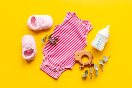 Pink baby bodysuit with wooden teethers and bottle of milk on yellow background, top view.の写真素材