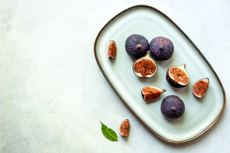Purple ripe figs and slices with leaves on a plate top view on a stone background.