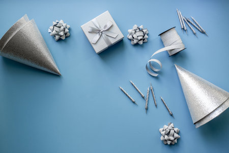Festive party decoration in silver color with gift box and carnaval caps on blue background, top view.の写真素材