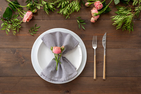 Top view of table setting with empty plate, cutlery and napkin - pink roses flowers decorated on...
