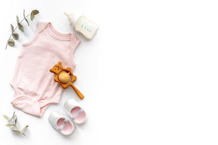 Flat lay of baby accessories - bodysuit and boots with wooden teether toys and bottle of milk on white background, top view.の写真素材