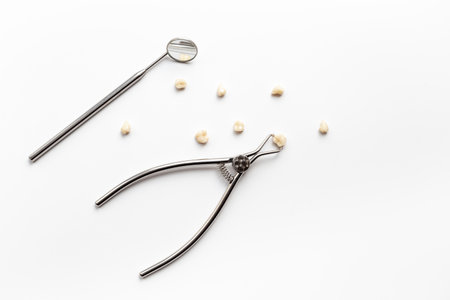 Many human teeth crown for dental implantation with tooth extraction forceps on white background. Professional Dentist tools, top view.の写真素材