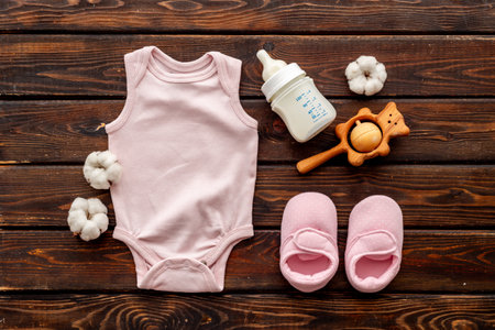 Flat lay of baby accessories - bodysuit and boots with wooden teether toys and bottle of milk on wooden background, top view.の写真素材