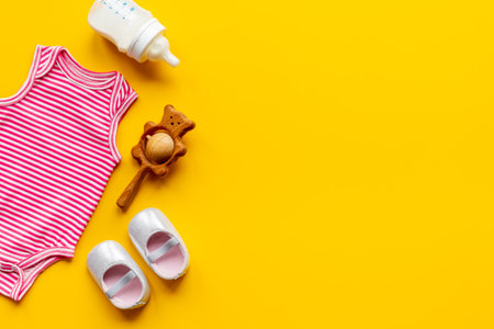 Pink baby bodysuit with wooden teethers and bottle of milk on yellow background, top view.の写真素材