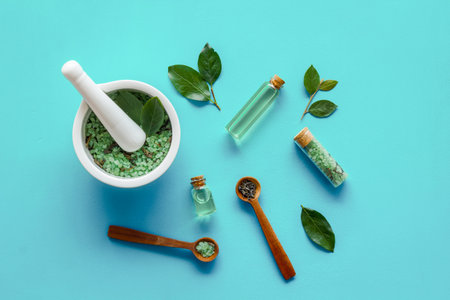 Homemade organic cosmetics products - tea tree essential oil and sea salt in mortar and pestle with green leaves on blue background, top viewの写真素材