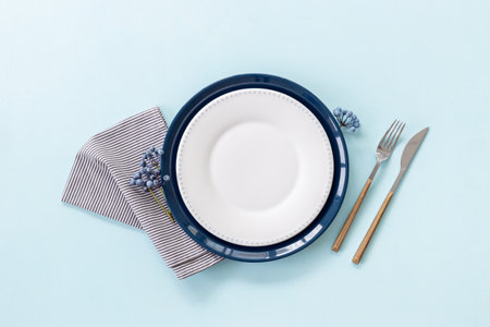 Beautiful minimalistic table setting with empty plate and napkin - blueberries decorated on blue background, flat lay. Top viewの写真素材