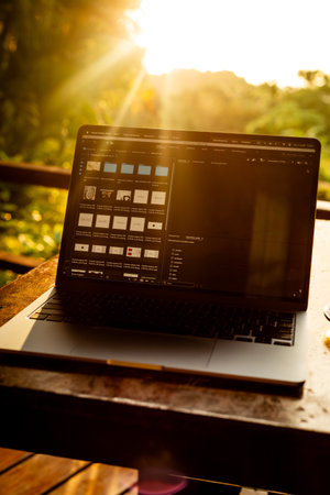 Laptop on wooden table with forest view at sunset, remote freelance work. Sunshine and backlightの写真素材