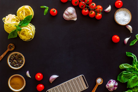 Frame of ingredients for cooking Italian pasta - uncooked fettuccine with tomatoes and basil leaves - on a black background, top viewの写真素材