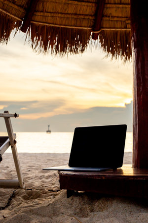 Digital nomad work place. Laptop on a beach sea coast at sunset.の写真素材