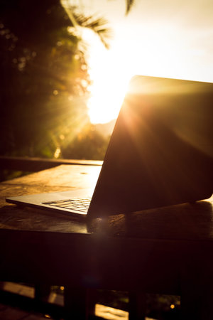 Laptop with backlight on wooden table on terrace in tropical forest at sunset, remote work digital nomadの写真素材