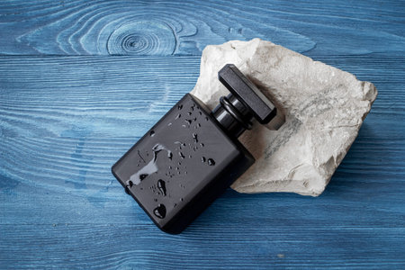 Stylish black perfume bottle with water drops. Male fragrance concept