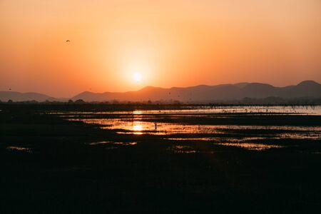 Peaceful sunset at small lake in Thailand with a mountain in the background.の写真素材