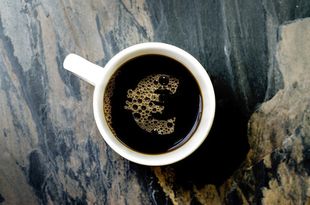 a euro symbol  this can serve as a concept for expensive coffee, caffeine addiction etc  and hands holding a cup of hot coffeeの写真素材