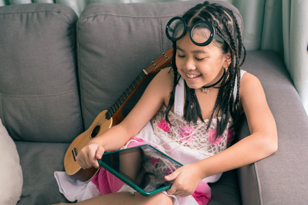 Cute little girl,wearing glasses,dreadlocks hair style ,playing with computer at home laying on sofaの写真素材