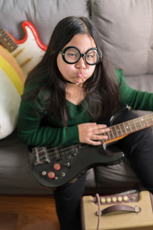 Happy smiling girl ,wearing glasses,learning to play the Bass guitarの写真素材