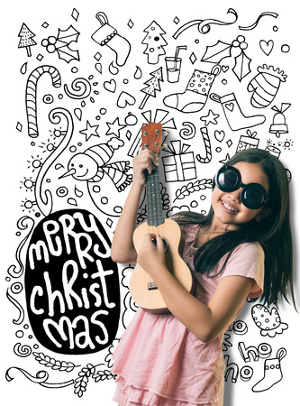 Cute little asian girl is playing guitar about Christmas ,Hand drawn Doodle about Christmas floating in the backgroundの写真素材