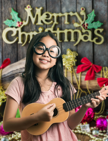 cute girl smiling and playing guitar in front of  Christmas and New Year decoration on wooden backgroundの写真素材