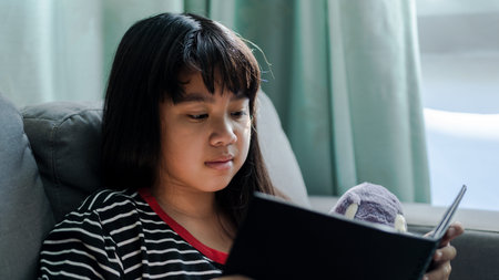 Cute  little girl  reading book her doll at home ,Soft focus shotの写真素材