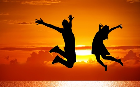 Silhouettes of couple jumping on sunset background の写真素材