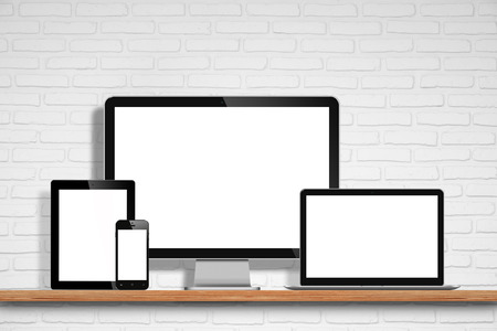 computer monitor, laptop, tablet pc and mobile phone with blank screen on the table with white brick wall backgroundの写真素材