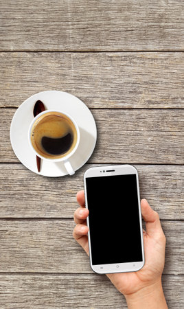Hand holding White Smart phone on wood coffee tableのeditorial素材