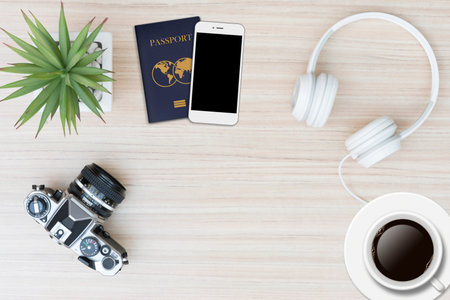 Top view of travel stuff. Camera, headphones ,passport ,mobile phone, and a cup of coffee on wood...