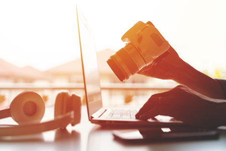 A freelancer working on laptop computer and holding DSLR Camera working from home or casual business...