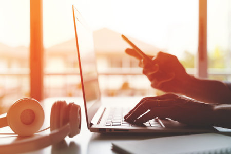 A freelancer working on laptop computer and holding smart phone working from home or casual business...