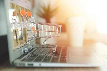 Online shopping concept, Shopping cart with blurry laptop on the deskの写真素材