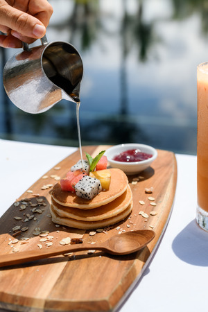 Stack of pancakes with honey syrup at pool side and glass of ice teaの写真素材