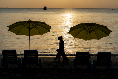 Silhouette couple of traveler walking through luxury yellow beach umbrella and beach chair setup on Kamala beach, Phuket, Thailand during sunsetの写真素材