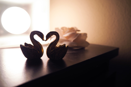 Feng shui swan figurines on bedside with rose and lamp in dark light. For love and romantic theme.