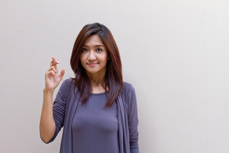 Woman with fingers crossed, plain blank background with text or copy space. Concept of wishing or praying for somethingの写真素材