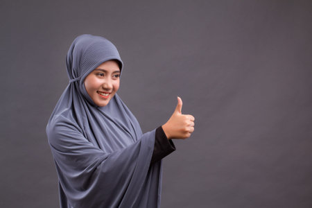 muslim woman pointing thumb up side way, asian islamic woman model