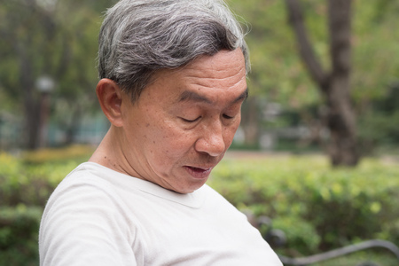sad hopeless frustrated old retired senior man sitting in public park, urban poverty conceptの写真素材