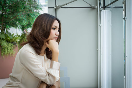 absent minded, stressed, unhappy sad woman looking out ot the office windowの写真素材