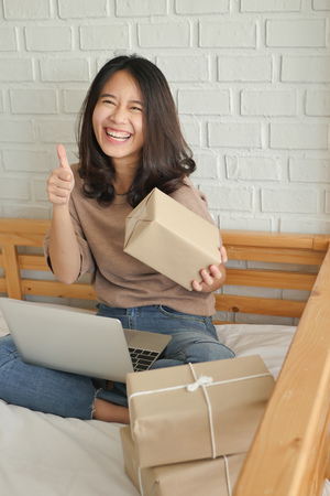 happy laughing joyful accepting woman giving thumg up gesture with computer and product parcel box at home, successful work at home merchandise delivery conceptの写真素材