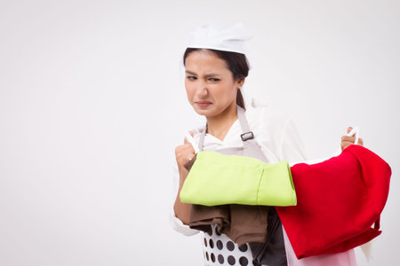 unhappy girl disgusted asian woman carrying stinking heavy laundry basket; portrait of domestic helper, woman housekeeper, sad woman maid holding laundry basket; girl cloth cleaning laundry service studio portraitの写真素材