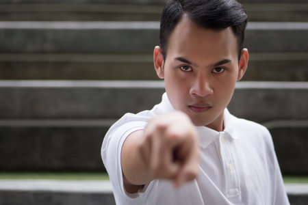 pointing man portrait; serious man pointing finger gesture; asian man points at you with serious mood emotion; young adult south east asian man model with tan skin and short hairの写真素材