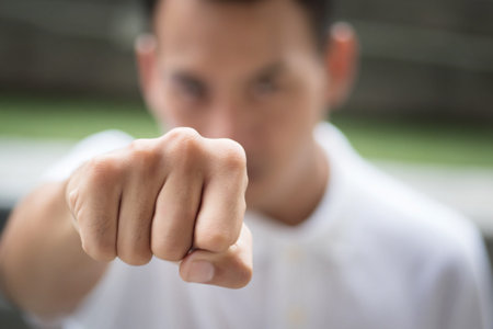 man punching; strong man clenching his fist portrait; man fighter in fist fighting pose looking at you; asian young adult man modelの写真素材