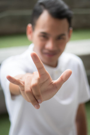 man with love or rock hand gesture; asian man showing love hand sign or rock hand sign; asian young...