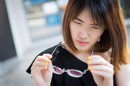 woman suffering from poor eye vision; portrait of asian woman with eye problem or bad blur eye sight holding eyeglasses, concept of seeing or visual disorder; young adult asian woman modelの写真素材